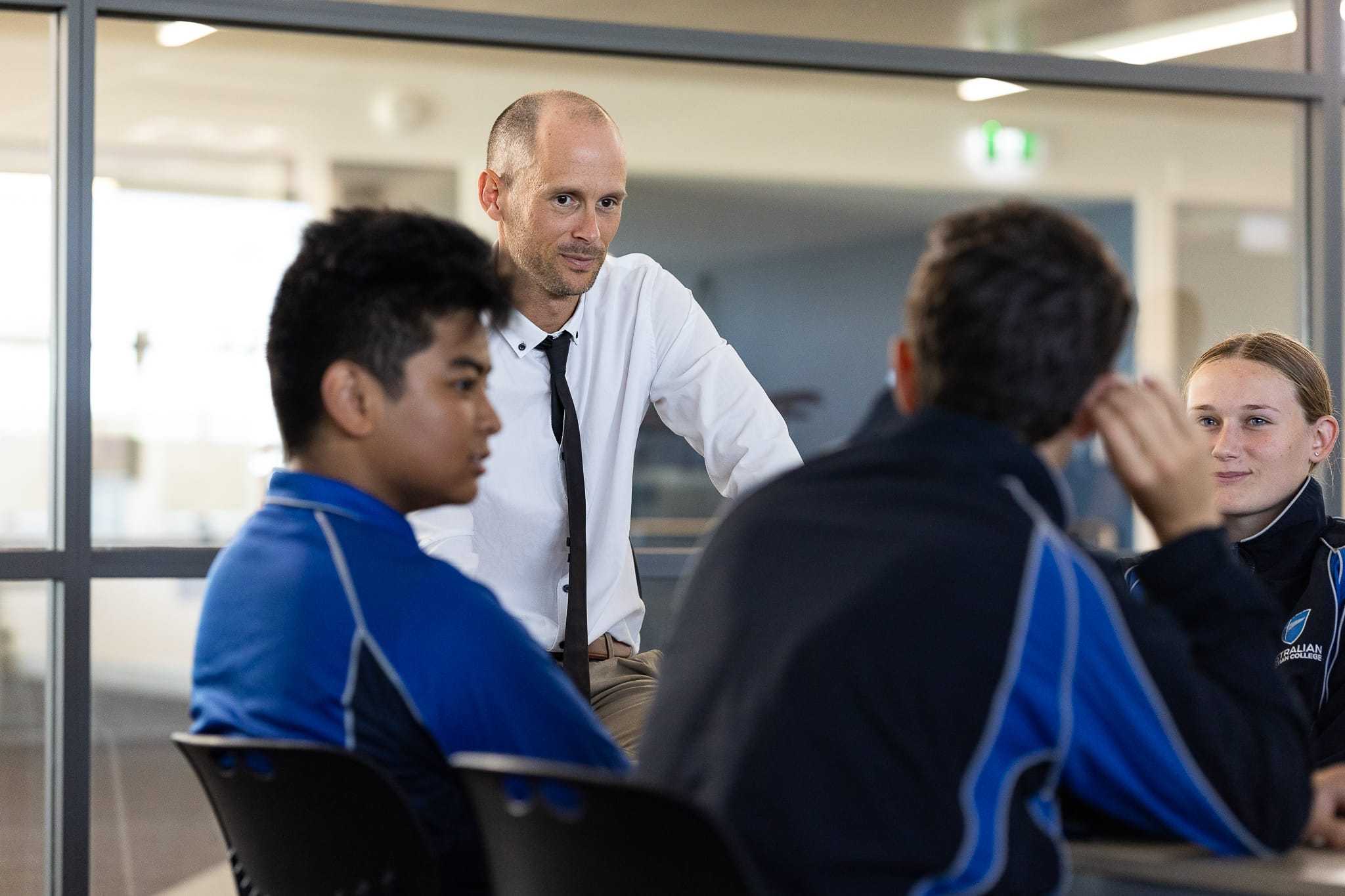 intern teacher with focused expression sitting at table listening intently to group of students