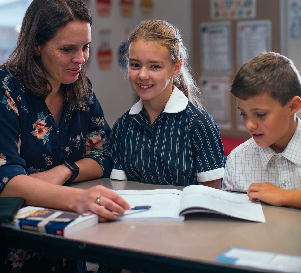 teacher sitting with happy young female student with open work book, helping them learn