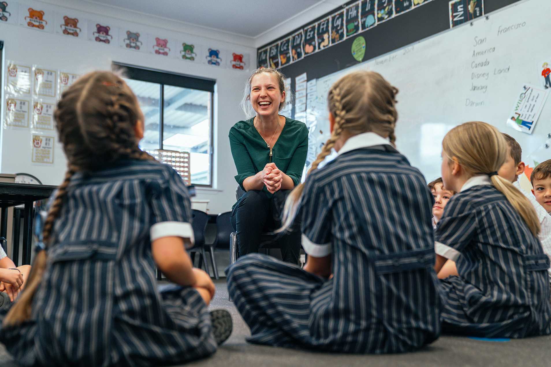 smiling happy female teacher sitting in front of class