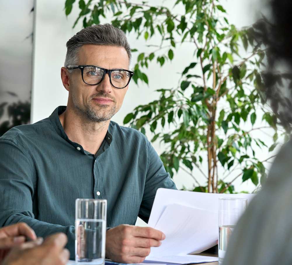 mature white male trainee principal wearing glasses sitting at table holding notes