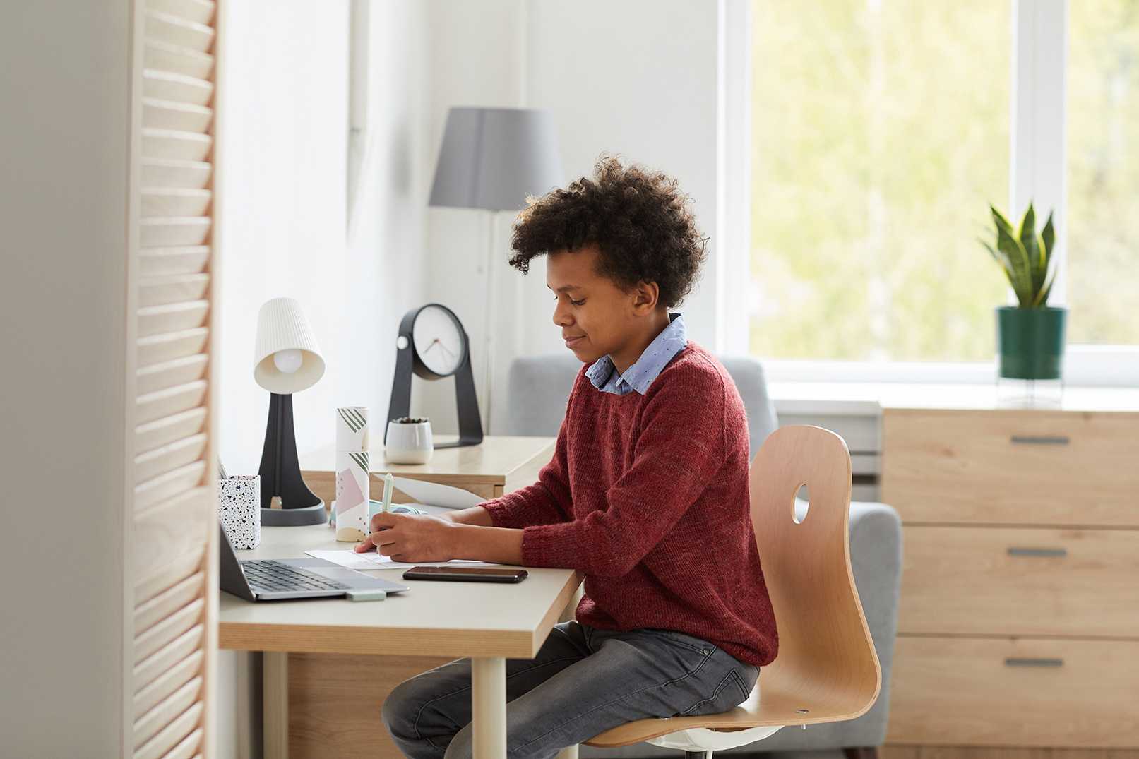 young black male Australian distance education student in red sweater completing school work at desk