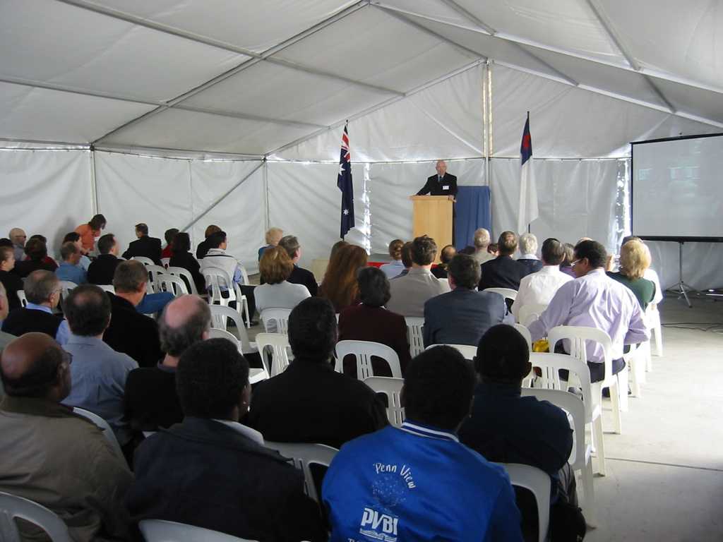 school board meeting inside white marquee tent with speaker with attendees listenting to speaker