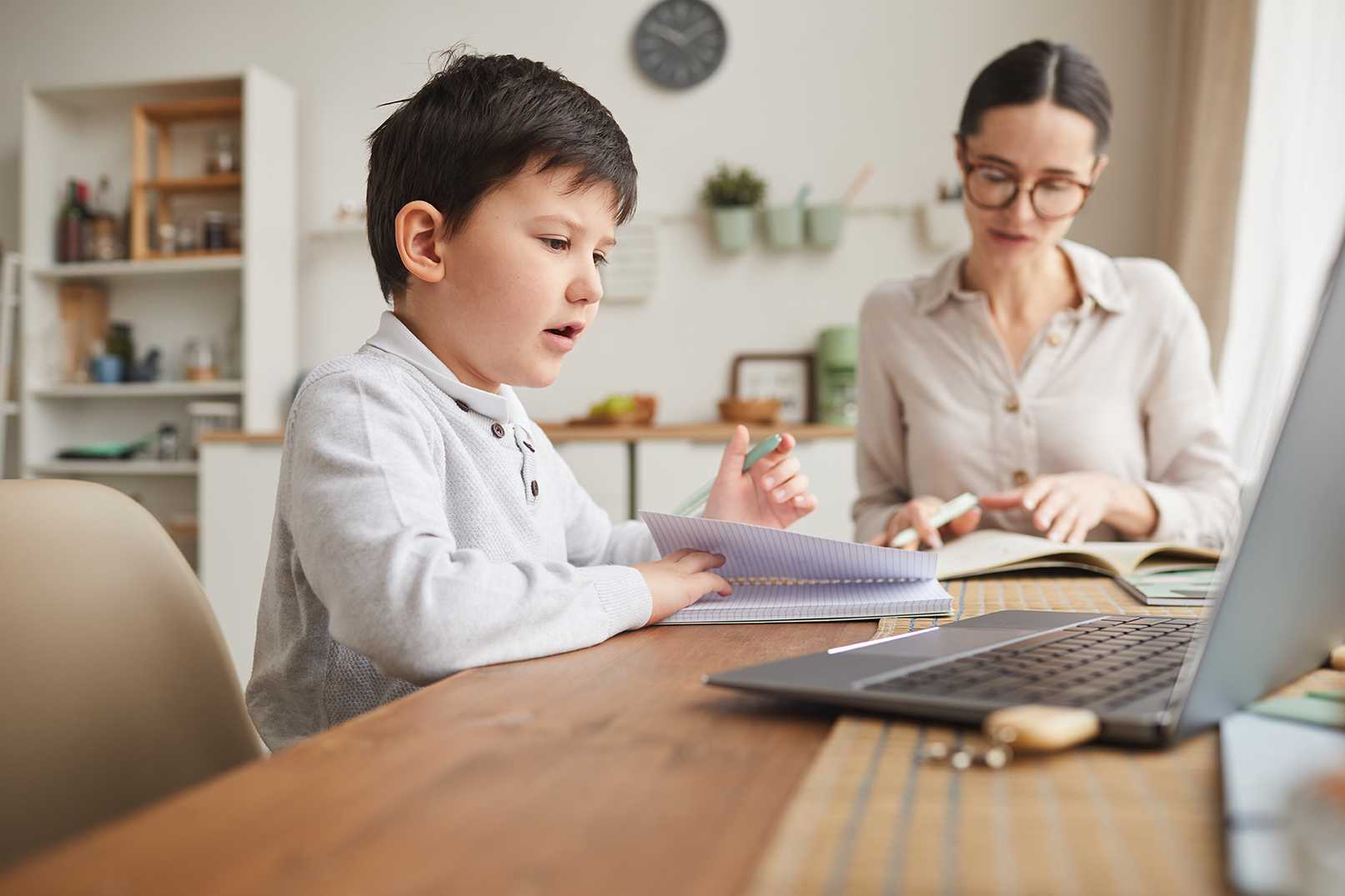 Australian home schooled boy completing work with laptop at table with mother supervising