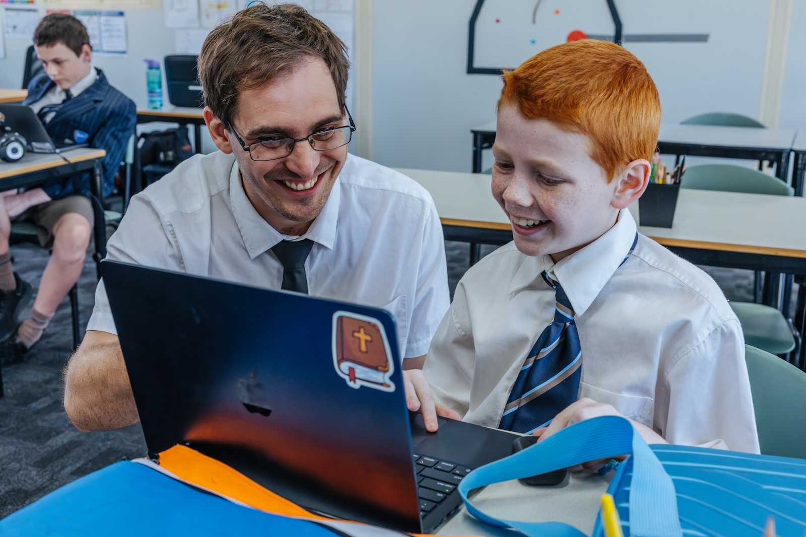 teacher sitting with happy young female student with open work book, helping them learn